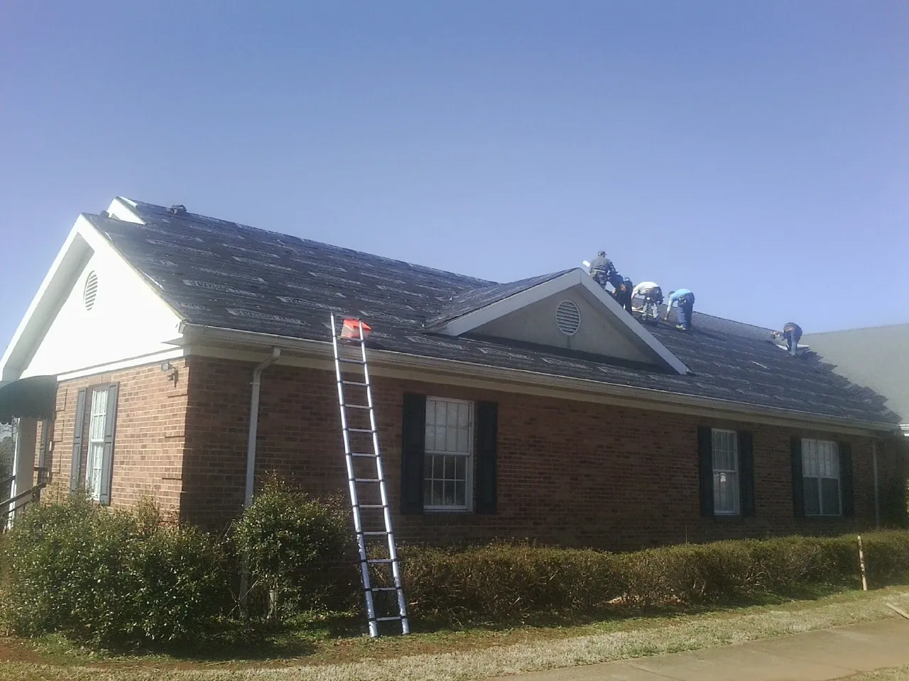 Crew tearing shingles off a brick ranch roof with a ladder set — Metal Roof Repair work by our crew in Lavallette