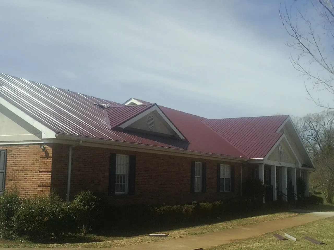 Red metal roof with gabled entries on a long brick building, from a Hail Damage Roof Repair job in Lavallette