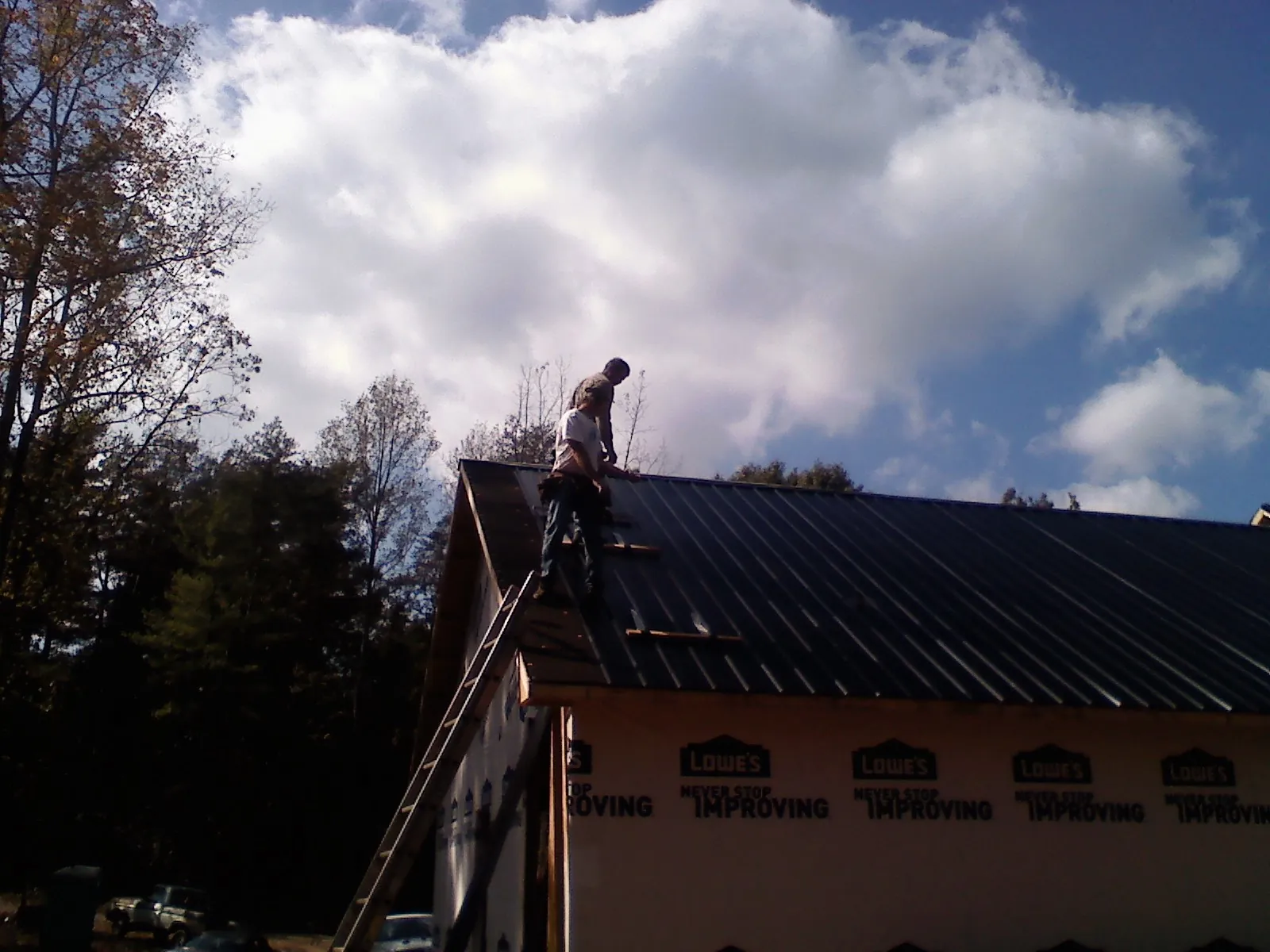 Roofer fastening dark metal panels high against a cloudy sky, from a Roof Inspection job in Lavallette