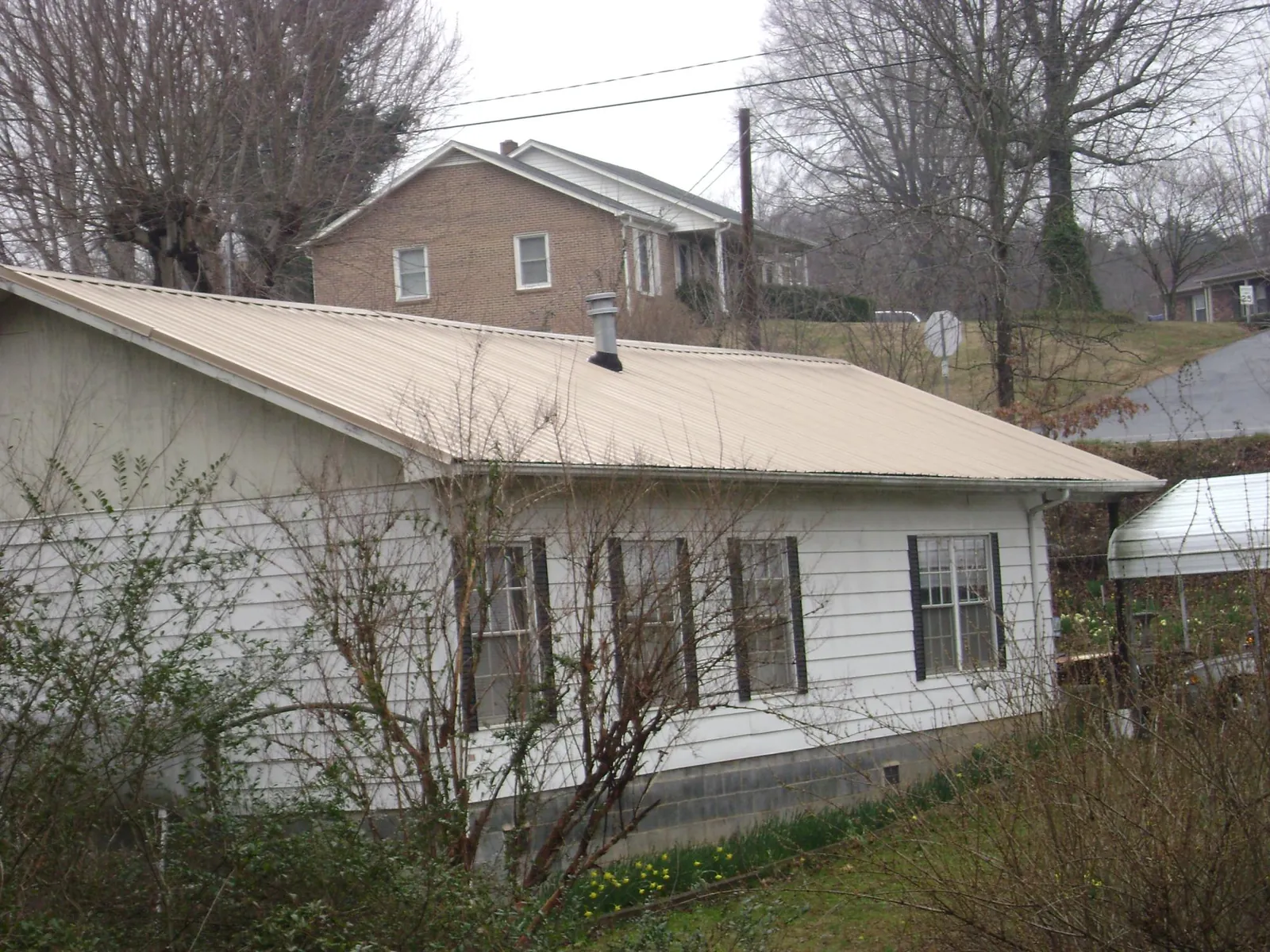 Tan metal roof on a white sided house set into a hillside — Commercial Roofing by Roofing Brothers in Lavallette